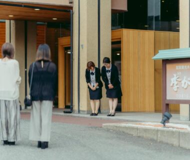 Two guests approaching Tokigasane entrance with staff bowing beside wooden facade and signboard
