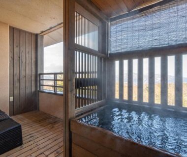 Wooden indoor soaking tub with slatted screens and distant mountain view at Tokinoniwa, Gunma