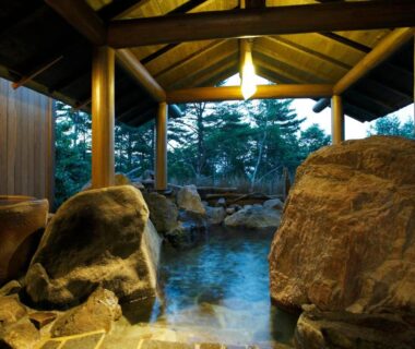 Covered outdoor rock onsen with wooden beams, large stones and trees at Tokinoniwa, Gunma, Kantō