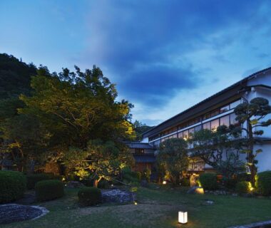 Evening exterior of Tokiwa Bekkan with illuminated garden lanterns, manicured shrubs and traditional Japanese architecture in Hyōgo