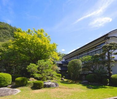 Manicured garden and lawn with trimmed shrubs in front of Tokiwa Bekkan building, Hyōgo mountains in background