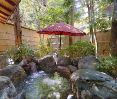 Outdoor stone onsen with red umbrella and bamboo fence at Tokiwa Bekkan, Hyōgo Kansai