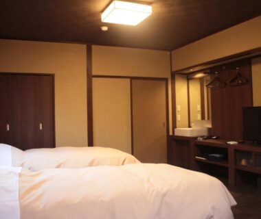 Twin beds with white duvets in traditional ryokan room with sliding doors, wooden furnishings, sink and TV in Tochigi