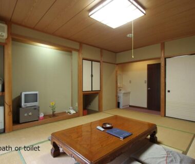 Tatami room with low wooden table, zabuton cushions and television at Tokonamiso Nagano