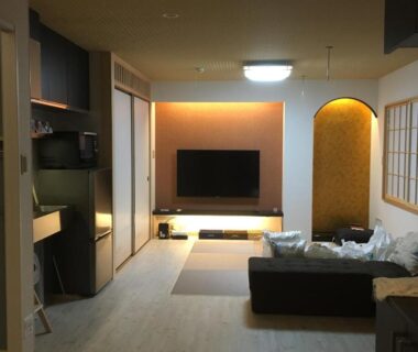 Modern ryokan living room with sofa, flat screen TV, shoji screens and kitchenette at Tokyo inn Sakura An