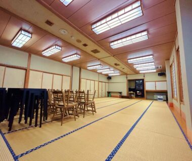 Spacious tatami hall with stacked chairs and low tables at Tomiya Ryokan Niigata