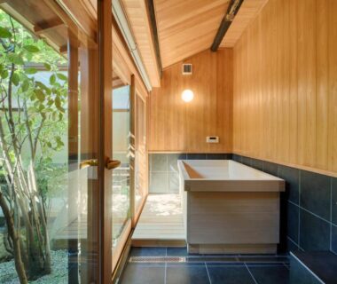 Wooden soaking tub beside glass doors opening to a courtyard garden at Tomonoura Shiomachi Hotel, Hiroshima