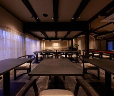Dimly lit dining hall with long wooden tables and exposed beams at Tomonoura Shiomachi Hotel, Hiroshima