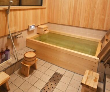 Wooden indoor onsen tub with stools and shower at Toshiharu Ryokan in Kyoto, Kansai