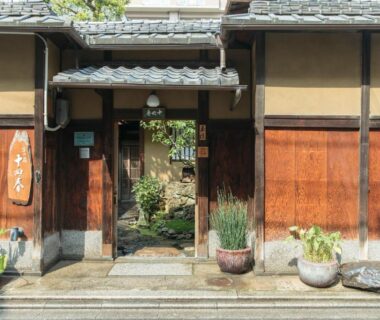 Wooden gate with potted plants and stone path leading to inner garden at Toshiharu Ryokan Kyoto