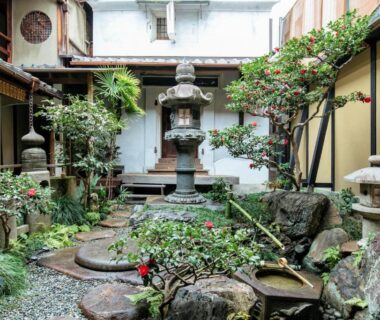 Stone lantern courtyard with stepping stones, moss and potted plants at Toshiharu Ryokan in Kyoto