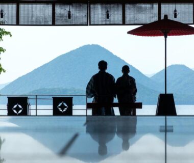 Two seated silhouettes by open window with red umbrella and reflective floor, Toya Kohan Tei, Hokkaidō