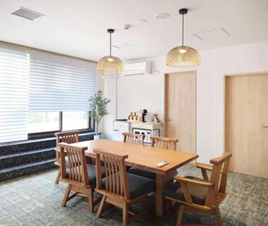 Communal dining table with wooden chairs, pendant lights, window seating and small kitchenette at Toya-onsen Hotel Hanabi in Hokkaidō