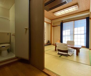 Tatami-floored room with low table, shoji screens and adjoining bathroom with toilet at Toyofuku in Hyōgo