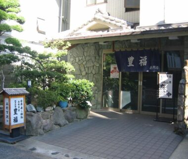 Traditional entrance with blue noren and stone facade at Toyofuku in Hyōgo small manicured garden