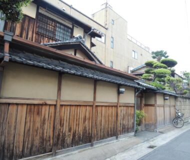 Long wooden exterior wall and tiled roof of Tsubakiso along narrow Nara street with a bicycle