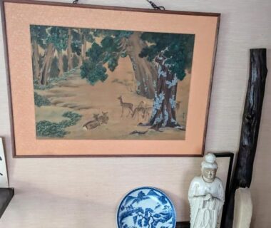 Framed woodland deer painting above blue porcelain plate and standing figurine on wooden shelf in ryokan interior Nara