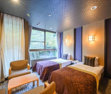 Twin room with two beds and seating by large window showing trees at Tsuetate Onsen Hotel Hizenya, Kumamoto