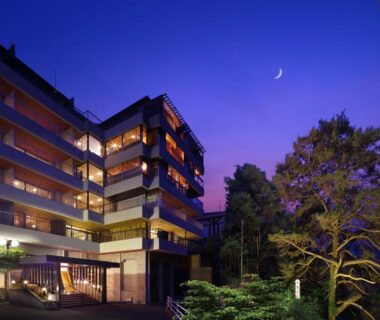 Dusk view of multi-story ryokan with lit balconies and landscaped trees at Tsuganoki in Tochigi