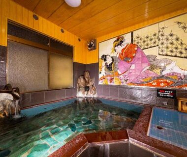 Hexagonal indoor onsen bath with decorative ukiyo-e mural and stone water spout at Tsukasa Ryokan Saga