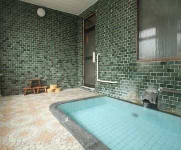 Tiled indoor bathing area with small stools at Tsukasaya Ryokan in Yamagata