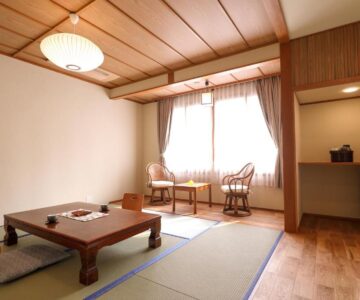 Traditional tatami room with low table, floor cushions, wooden ceiling and window seating at Tsukasaya Ryokan, Yamagata