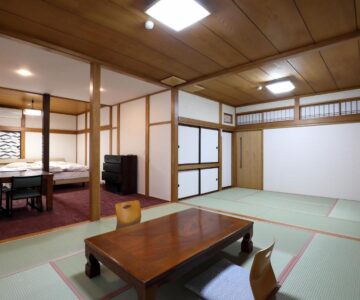 Spacious tatami room with low wooden table, shoji screens and adjacent dining area at Tsukasaya Ryokan, Yamagata