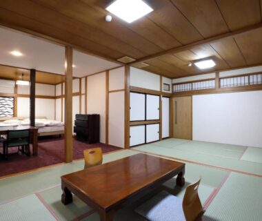 Spacious tatami room with low wooden table, shoji screens and adjacent dining area at Tsukasaya Ryokan, Yamagata