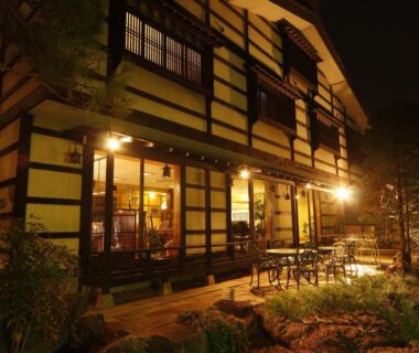 Illuminated traditional ryokan exterior with wooden veranda and garden at night, Tsuki no Shizuka, Nagano