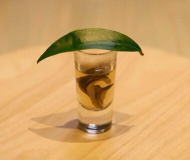 Glass with swirling liquid covered by a green leaf on a wooden table at Tsuki to Maguro Ishigami Shizuoka