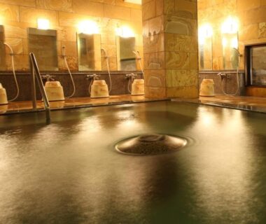 Steamy indoor onsen with central stone pool, tiled walls and wooden washing stools with buckets at Tsuruya Ryokan Nagano