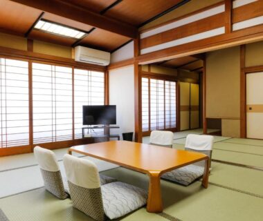 Spacious tatami room with low table, floor chairs, shoji screens and TV at Tsuruya Ryokan in Hyōgo, Kansai