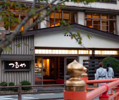 Guests in yukata at wooden ryokan entrance near red bridge in Hyōgo Kansai