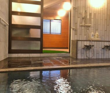Tiled indoor onsen with soaking pool, wall-mounted showers and wooden partition at Tsutaya Ryokan Hyōgo