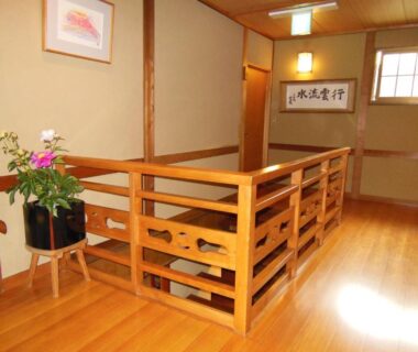 Polished wooden corridor with railing, calligraphy hanging and potted flowers at Tsutaya Ryokan, Hyōgo