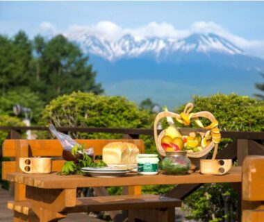 Outdoor wooden table with breakfast spread, fruit basket and cheese at Tsutaya Tokinoyado Kazari in Nagano mountains
