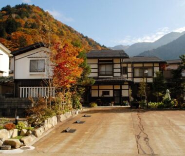 Traditional ryokan entrance with autumn foliage and mountain backdrop at Tsuyukusa in Gifu prefecture