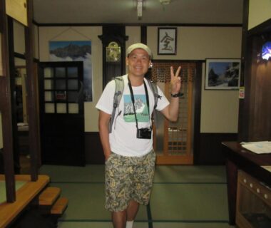 Traveler standing on tatami floor in ryokan lobby with shoji screens and wooden furnishings at Tsuyukusa, Gifu