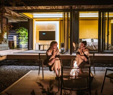 Guests wearing robes relaxing around an outdoor fire pit beside a modern villa with illuminated rooms at night, Shizuoka