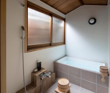 Tiled soaking tub with hand shower, wooden stools and frosted window in UTAHI A Kyoto machiya bathroom