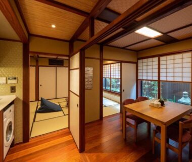 Interior with tatami room, wooden dining table, shoji screens and compact kitchenette with washing machine at UTAIMACHI, Ishikawa