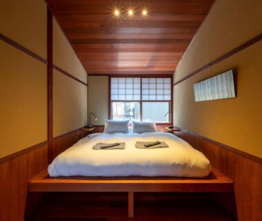 Raised futon-style bed with shoji window and folded linens at UTAIMACHI, Chūbu Ishikawa