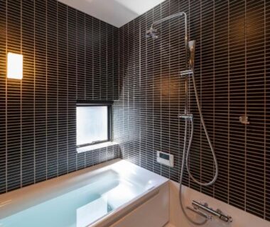 Bathtub with shower and dark tiled wall in UTAIMACHI ryokan bathroom, Ishikawa Chūbu