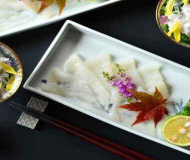 Plated sashimi on a rectangular dish with edible garnishes, citrus wedge and chopsticks
