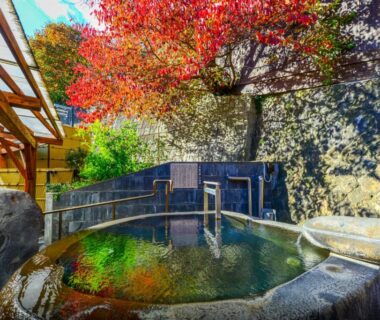 Stone outdoor onsen pool framed by red maple foliage at Uesugi no Miyu in Yamagata, Tōhoku