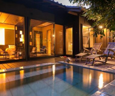 Outdoor bath terrace with wooden chairs, glass doors and warm interior lighting at Ufufu in Shizuoka