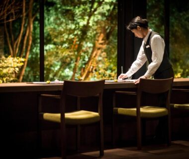 Attendant arranging items on wooden counter with garden view at Ufufu ryokan in Shizuoka Chūbu