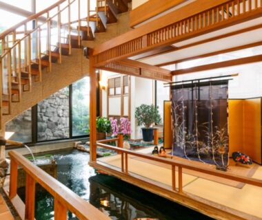 Wooden walkway over interior pond with noren divider, staircase and plants at Umemura Ryokan, Nagano
