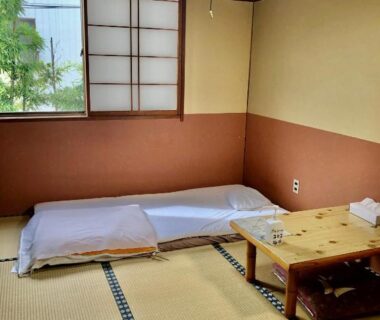 Traditional tatami room with futon, shoji window and low wooden table at Umeoka Ryokan in Nagano