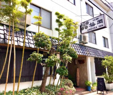 Building facade with entrance, potted plants, bamboo and sign for Umeoka Ryokan in Nagano